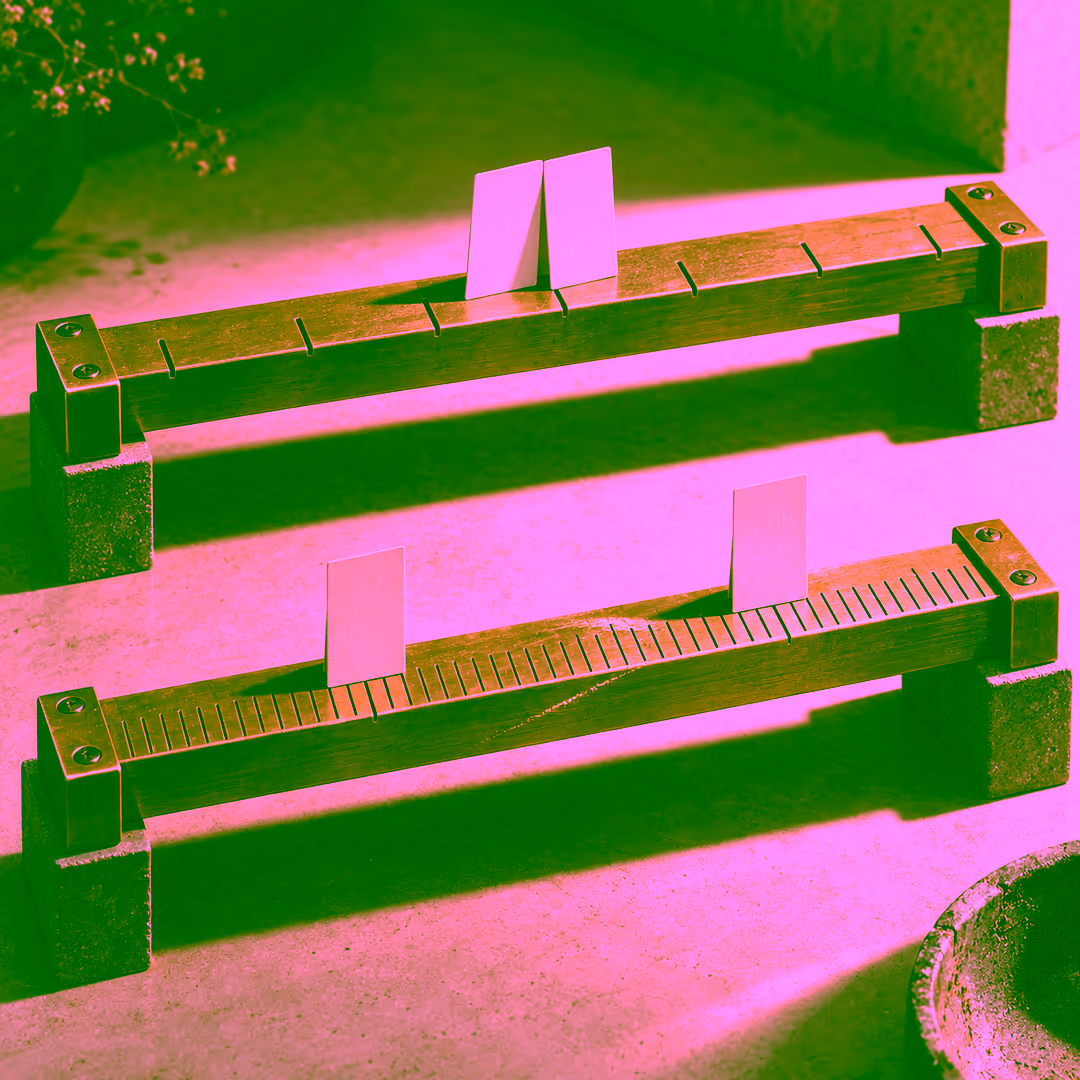 Two brass measuring rails. On the coarse upper rail two identical blank cards rest on the very same notch and lean together; on the finely graduated lower rail the same two cards stand clearly apart.