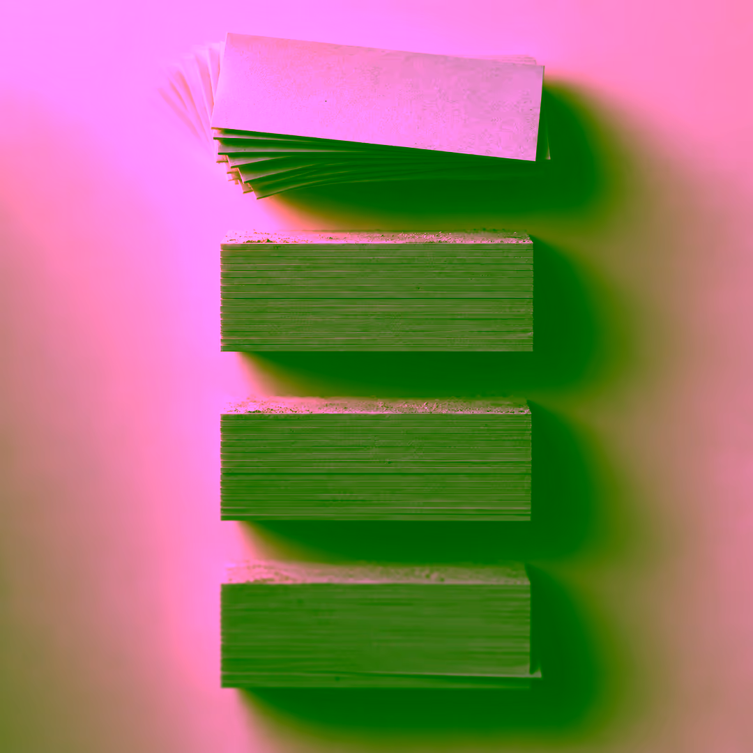 A column of four stacks of blank cards. Only the top stack is fanned apart and catching warm light; the three stacks below are squared off, matte and dusted along their top edges.